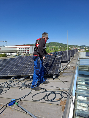 Mitarbeiter reinigt aufgeständerte PV-Paneele auf dem Dach von Neidlinger Kunststoffe.
